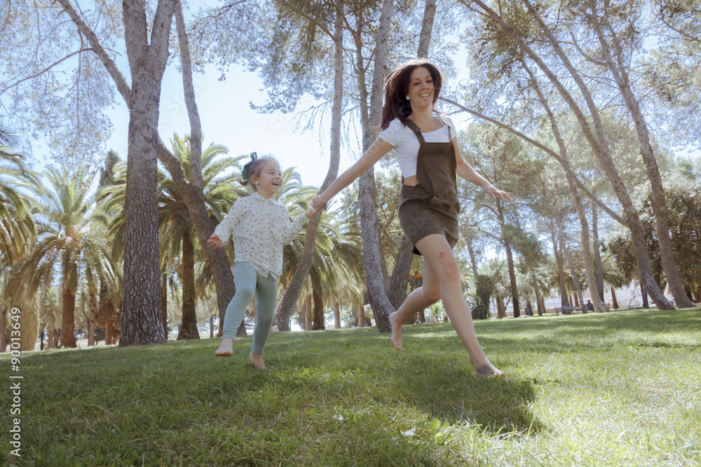 Una niña y su mama corriendo por el parque. Madre e hija jugando en el parque. Una niña y su mama disfrutando del verano rodeadas de árboles. Madre joven soltera.