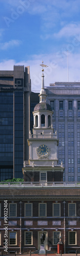 This is a vertical view of the top of historic Independence Hall, the site of the signing of the Declaration of Independence and the U.S. Constitution. A small dome and clock are seen toward the top. There is blue sky above the dome. photo