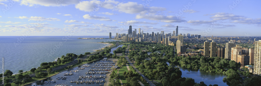 This shows Lincoln Park, Diversey Harbor with its moored boats, Lake Michigan to the left and the skyline in summer. There is morning light on the city.