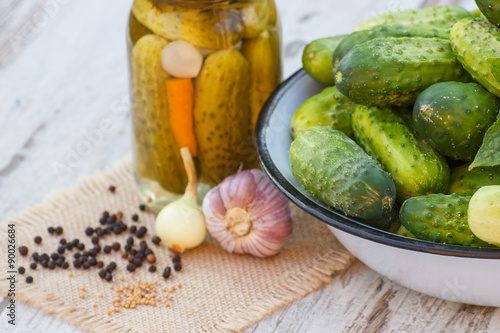 Cucumbers in metal bowl, spices for pickling and jar pickled cucumbers on table