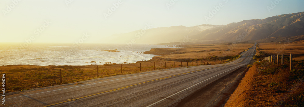 Fototapeta premium To jest trasa 1 znana również jako Pacific Coast Highway. Droga znajduje się obok oceanu, z górami w oddali. Droga zmierza w nieskończoność w zachód słońca.