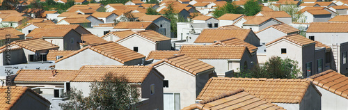 This is a housing development in a Southern California desert community. The houses have reddish orange Spanish tile roofs. They are situated very close to each other and they all look identical. There are a few trees in between the homes. photo