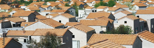 This is a housing development in a Southern California desert community. The houses have reddish orange Spanish tile roofs. They are situated very close to each other and they all look identical. There are a few trees in between the homes.