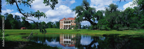 This is a southern plantation called Drayton Hall. It is a pre-Revolutionary plantation set on the Ashley River. It has Georgian Palladian architecture and was built from 1738-1742. It is set back on a green lawn with a pond showing the reflection of the plantation in the water.