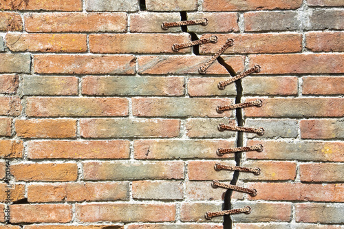 Billede på lærred Cracked brick wall with with a metal seam - concept image