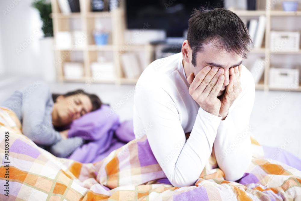 Man Awake In Bed Suffering With Insomnia. Woman sleeping in the Man Awake In Bed Suffering With Insomnia. Woman sleeping in the