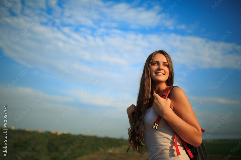 Young woman with red backpack walking on sunset summer.