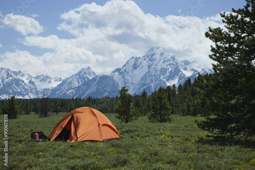 Orange tent in meadow below Grand Teton mountain range