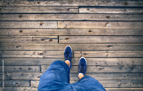 A man walking on aged wooden floor, point of view perspective. A man with blue shoes and shorts jeans walking alone on old wooden bridge. Conceptual photo, point of view perspective used.  photo