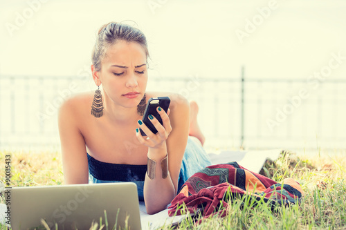 Canvas Print sad skeptical unhappy serious woman texting on phone outdoors in park