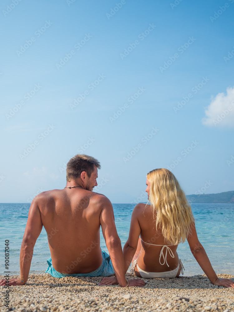 Young couple sitting together on a sand by sea and looking to a Young couple sitting together on a sand by sea and looking to a