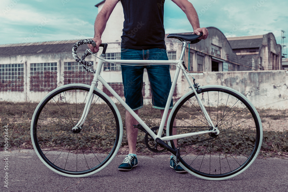 Naklejka premium Young man with a fixie bike. Decadent industrial setting