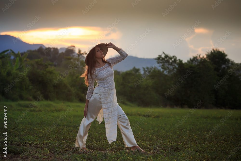 blonde girl in Vietnamese dress looks into distance on field