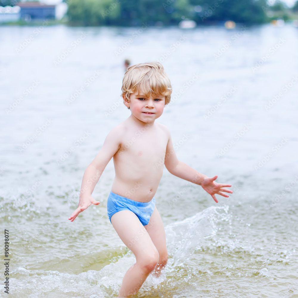 Little blond kid boy having fun with splashing in a lake, outdoo Little blond kid boy having fun with splashing in a lake, outdoo