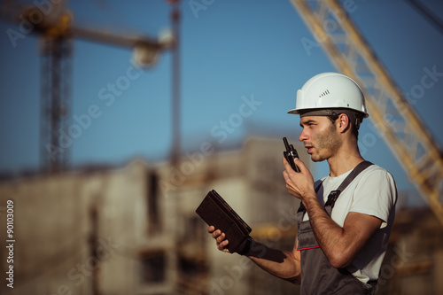 Engineer builder using a walkie talkie giving instructions at construction site. photo