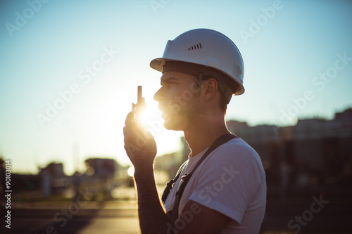 Engineer builder using a walkie talkie giving instructions at a construction site. Sunset time. photo