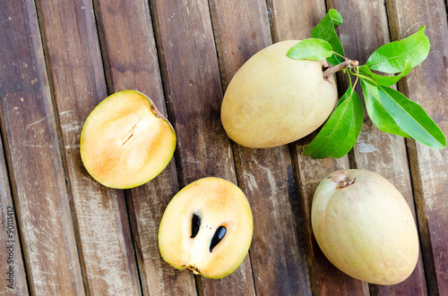 Fresh sweet sapodilla fruit with leaves on wooden background photo