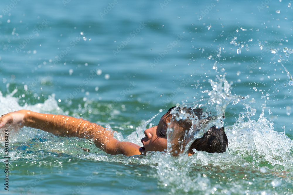 Ten year old boy teenager swims in the sea with big splashes