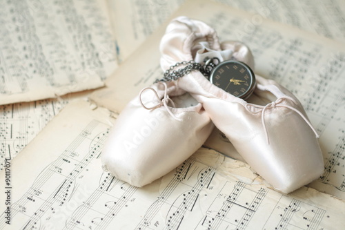 Ballet shoes and old watch laying on the old piano musical notes