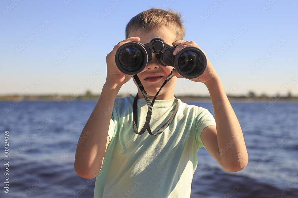 watching through binoculars. Boy looks through binoculars at the river, the position of a full-face watching through binoculars. Boy looks through binoculars at the river, the position of a full-face