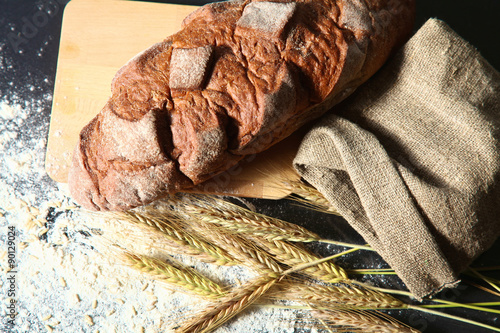 rustic crusty bread and wheat ears on a dark wooden table