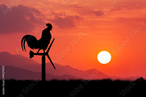 Roosters crow stand on a wind turbine. In the morning sunrise ba
