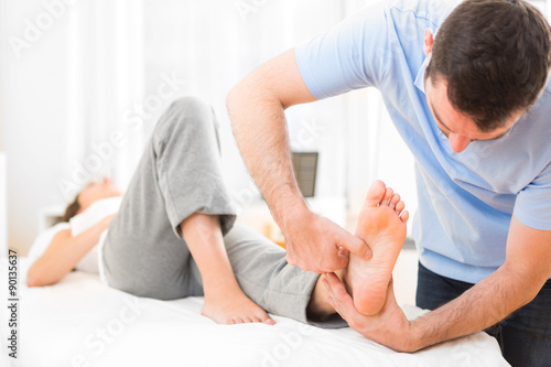 Young attractive physiotherapist doing reflexology on a patient