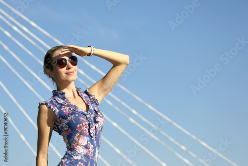 young beautiful girl in sunglasses looking at the sun on the blue sky background