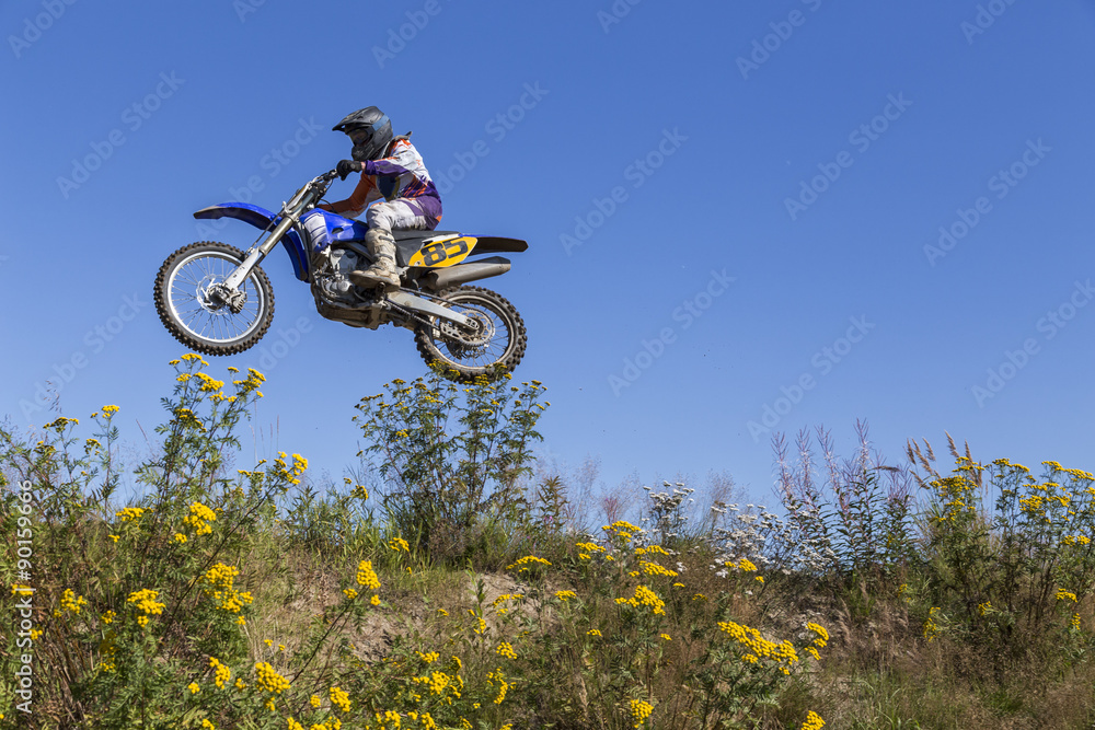 A man jumping with his motorcycle from a low angle and vegetation in the foreground
