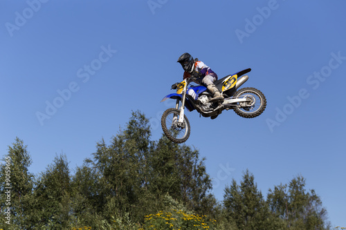A man jumping on his motorcycle and some trees in the background