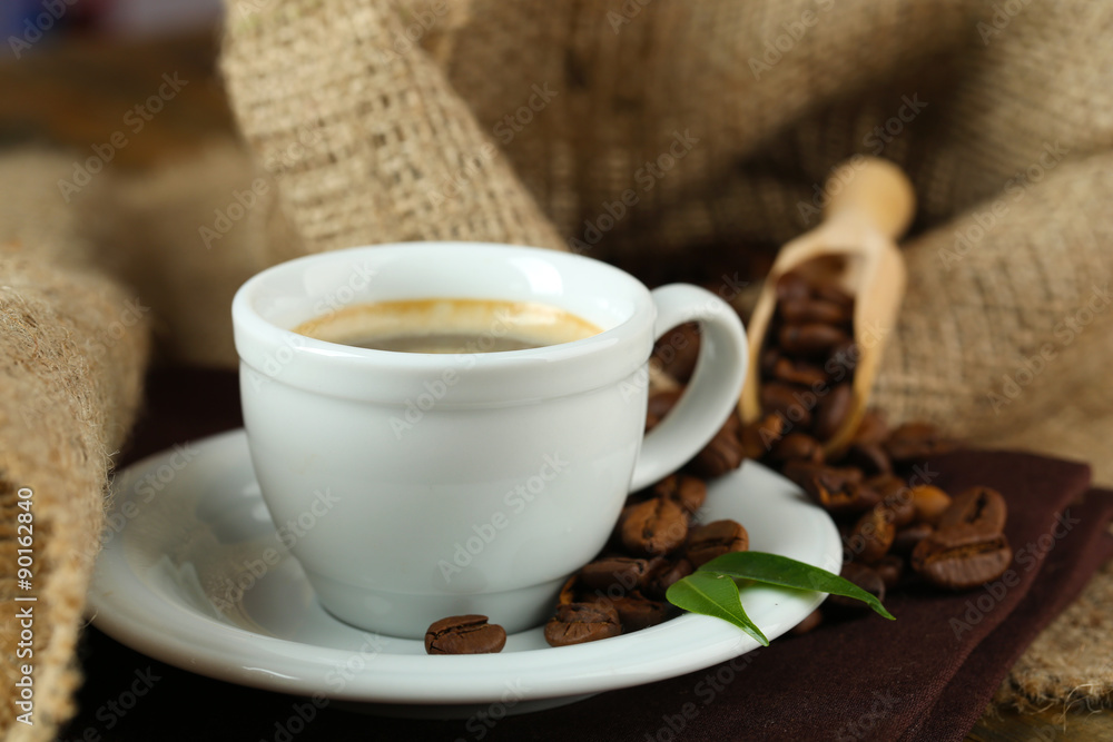 Fototapeta premium Cup of coffee with beans on table close up