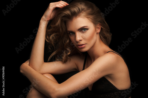 Vogue style close-up portrait of beautiful woman with long curly blond hair on black background