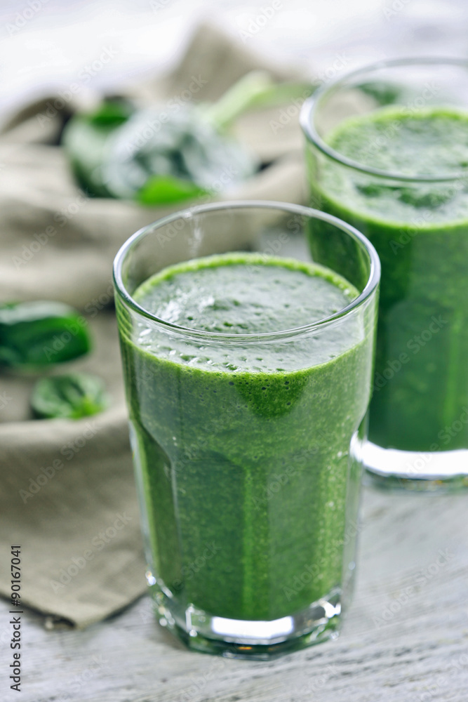 Fototapeta premium Glasses of spinach juice with napkin on wooden table, closeup