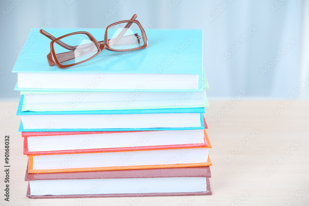 Stack of books with glasses on wooden table in room Stack of books with glasses on wooden table in room