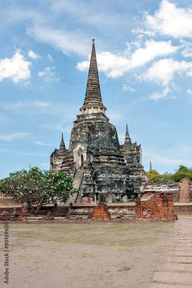 Ancient Buddhist temple in Ayutthaya. Thailand. Blackened by time stands among the ruins of the temple against the blue sky with clouds. Bright sunny day.