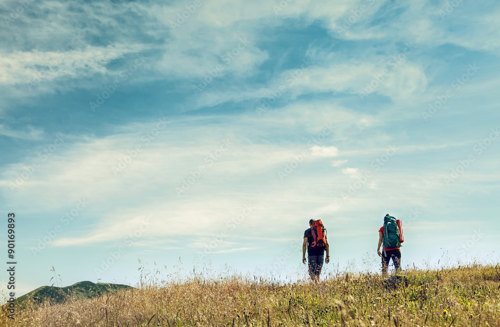 Two mountain travelers with backpacks under blue sky Two mountain travelers with backpacks under blue sky