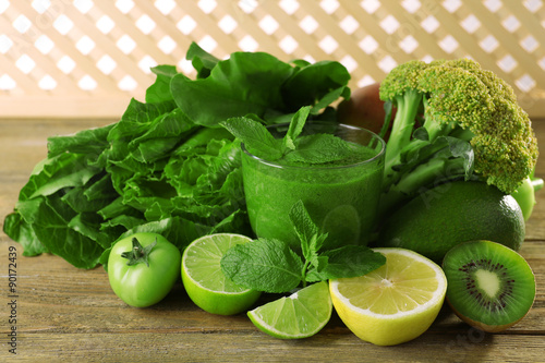 Green healthy juice with fruits and vegetables on wooden table close up