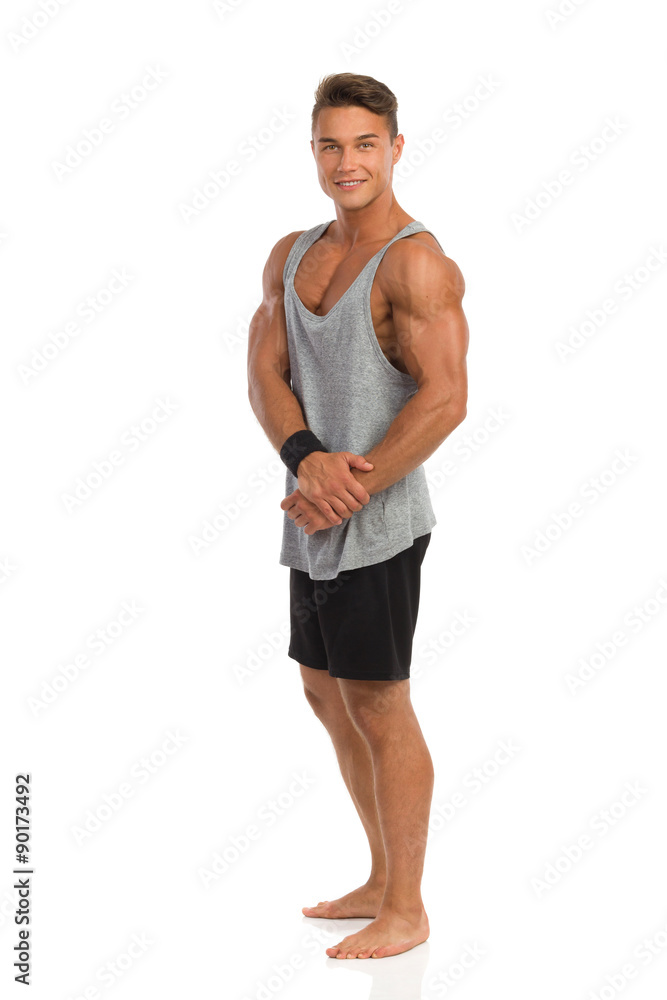 Fit Man Posing. Happy muscular man in gray shirt and black shorts standing barefoot. Full length studio shot isolated on white. Fit Man Posing. Happy muscular man in gray shirt and black shorts standing barefoot. Full length studio shot isolated on white.