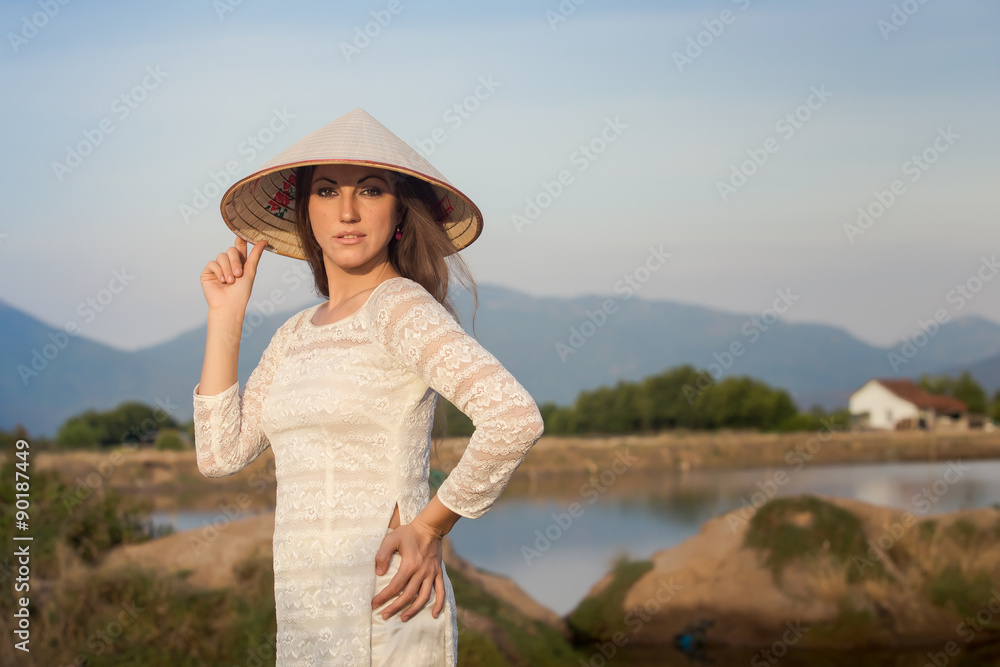 blonde girl in Vietnamese dress smiles against country lakes