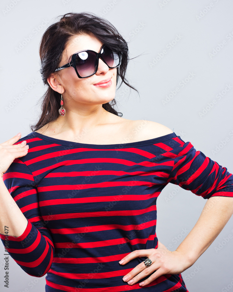 Naklejka premium Beautiful brunette in a blue dress with red stripes. Fashion. Portrait of a young girl in sunglasses. 