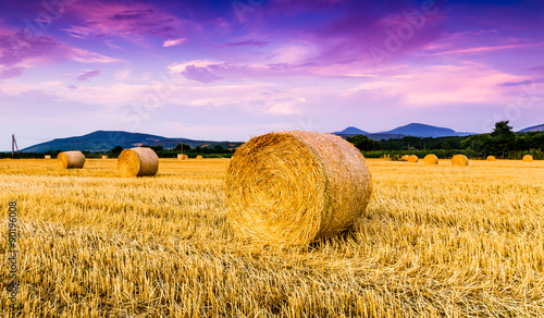 Golden sunset over farm field with hay bales photo