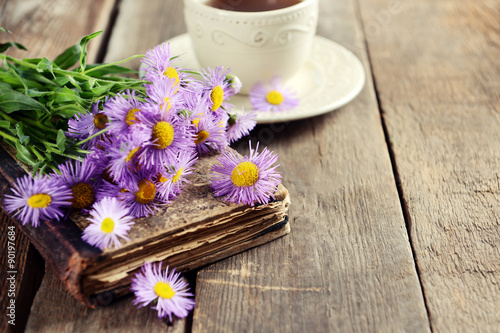 Old book with beautiful flowers and cup of tea on wooden table close up