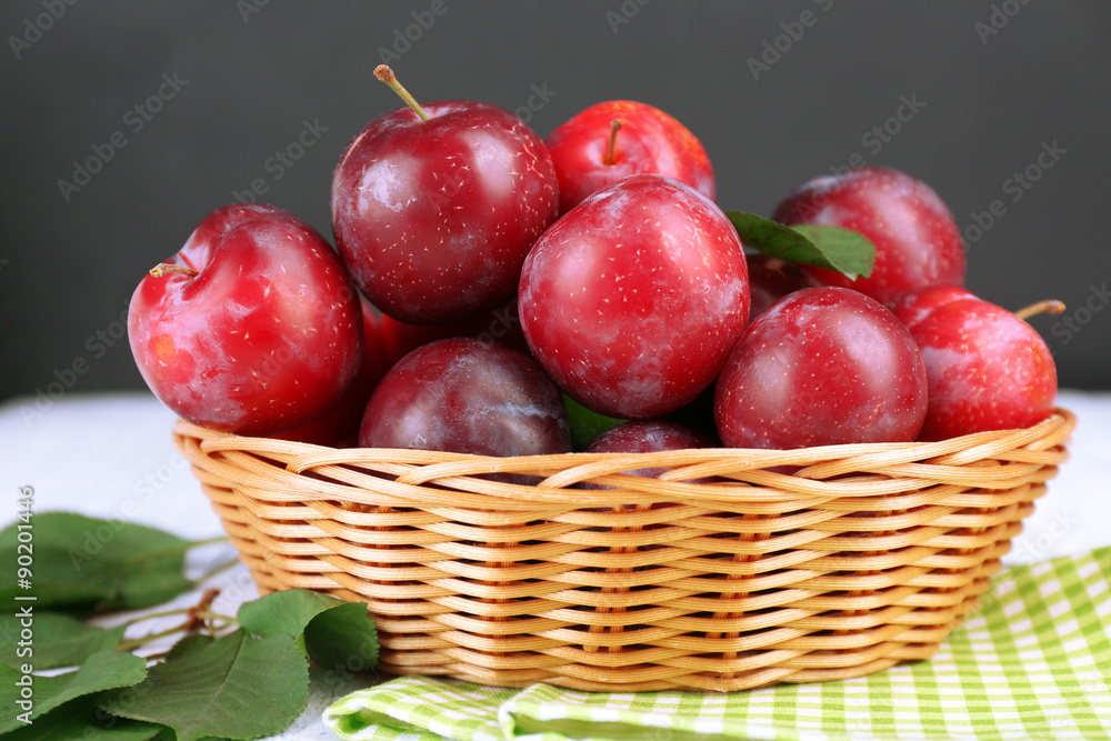 Ripe plums in wicker bowl on wooden table with napkin on dark background Ripe plums in wicker bowl on wooden table with napkin on dark background