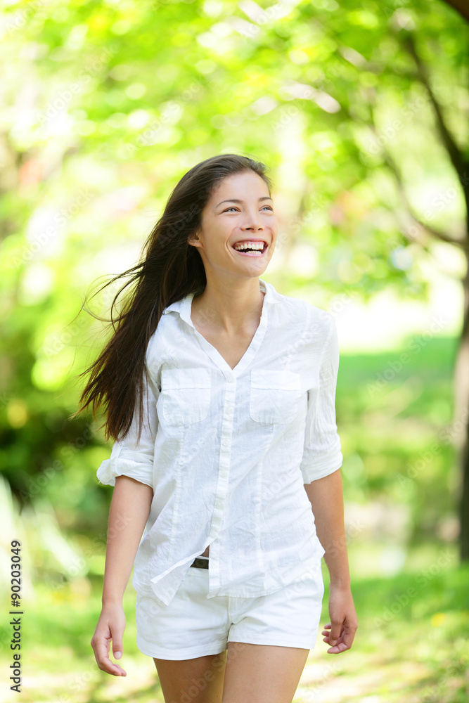 Happy young woman looking away. She is in casuals. Mixed race Asian / Caucasian female is walking in park.