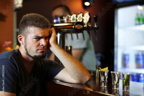 Young drunk man drinking tequila in bar