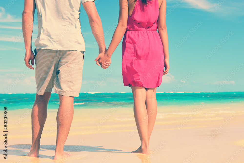 Low section of multiethnic couple holding hands on shore. Loving young tourists are standing at beach. They are spending leisure time together. Low section of multiethnic couple holding hands on shore. Loving young tourists are standing at beach. They are spending leisure time together.