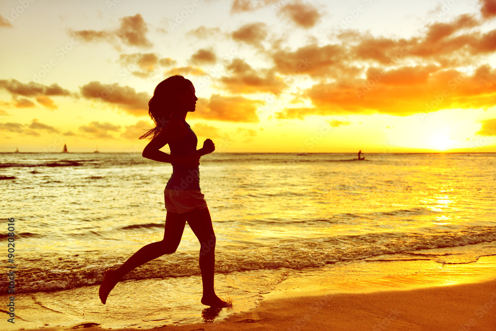 Full length of silhouette young woman jogging on shore. Side view of determined mixed race Asian / Caucasian female is running during sunrise. She is representing her healthy lifestyle.