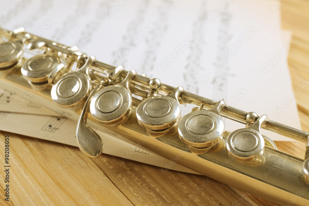 Naklejka premium Silver flute with music notes on wooden table close up