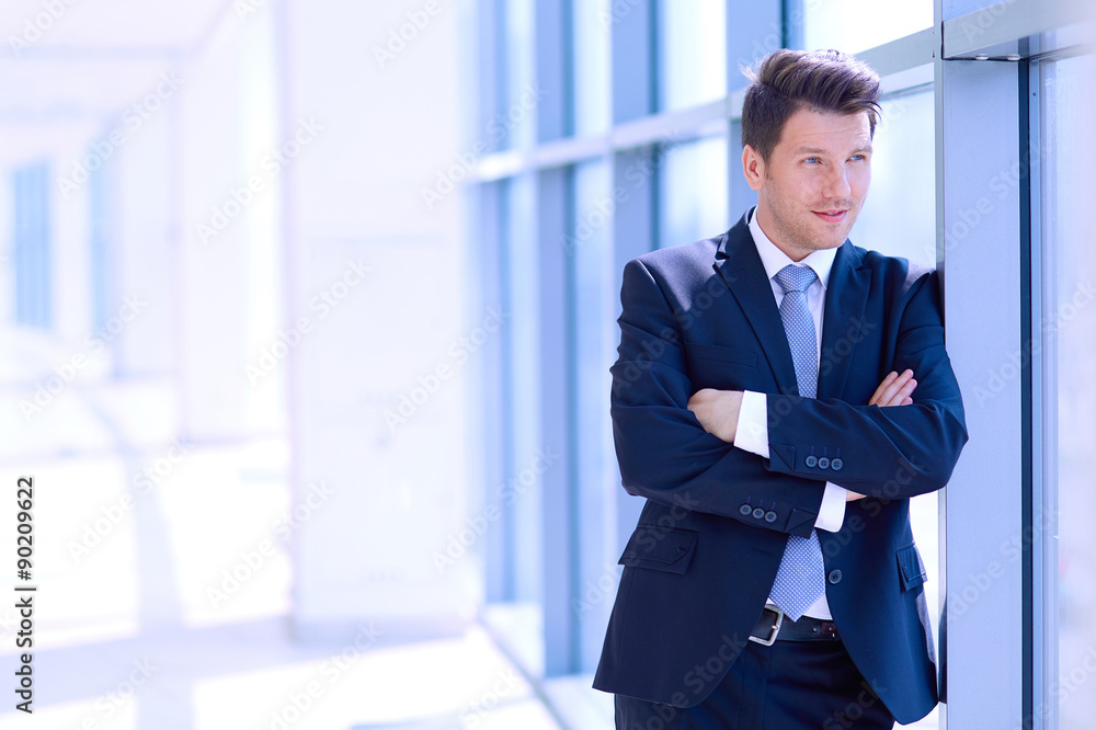 Portrait of businessman standing near window in office Portrait of businessman standing near window in office