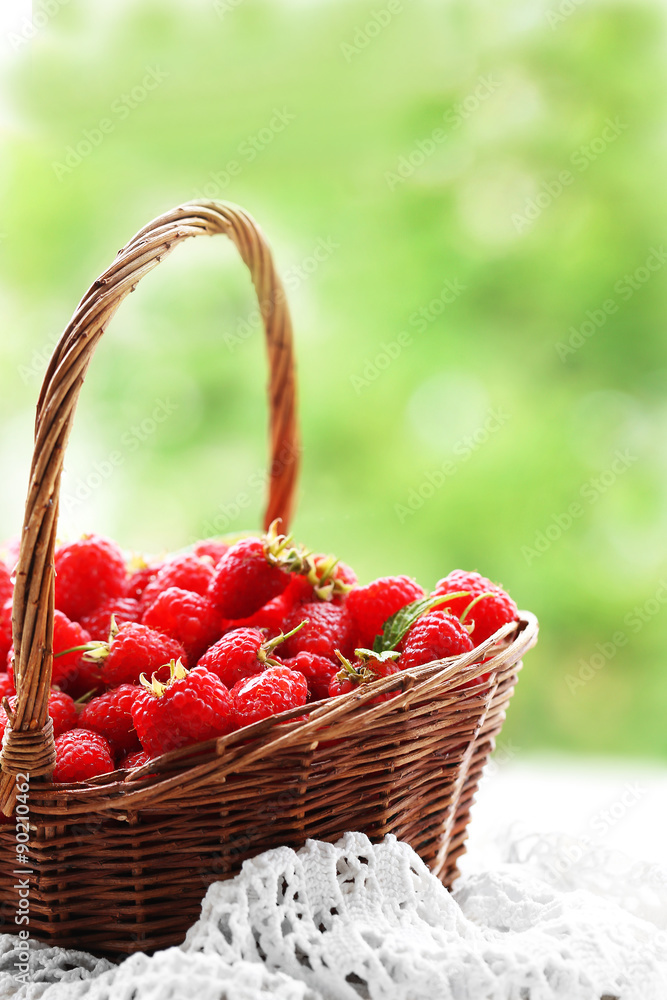 Fresh raspberries in wicker basket on wooden table on blurred nature background Fresh raspberries in wicker basket on wooden table on blurred nature background